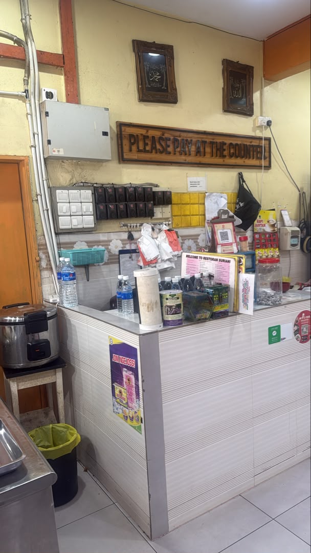 Papan kayu bertulis Please Pay At The Counter di dalam Restoran Suriani